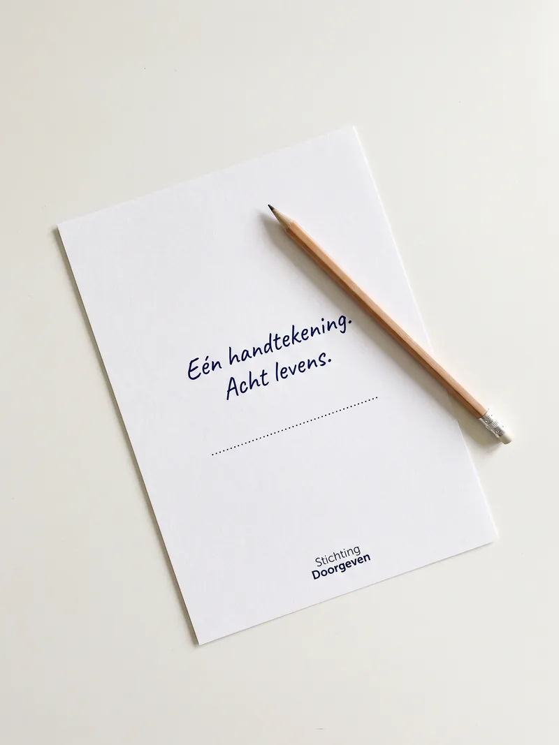 Wit vel papier met potlood en de handgeschreven tekst Eén handtekening, acht levens voor Stichting Doorgeven