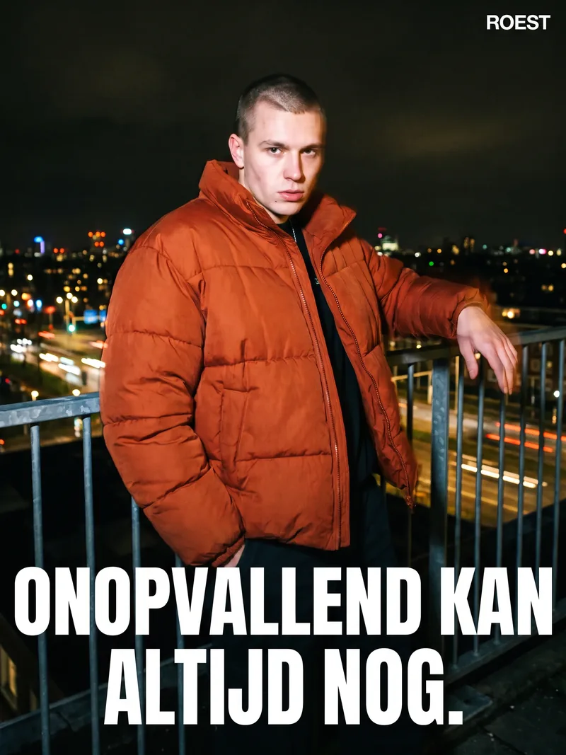 Jonge man in een roestoranje pufferjas op een dak in de nacht, geflitst, met de kop Onopvallend kan altijd nog voor Roest